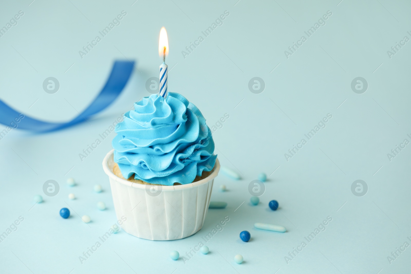 Photo of Birthday cupcake with burning candle on light blue background. Space for text