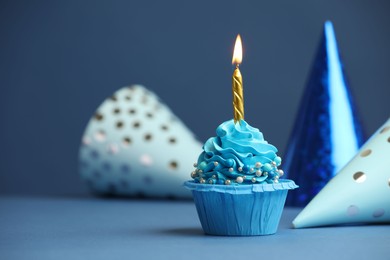 Photo of Birthday cupcake with burning candle and party cones on blue table