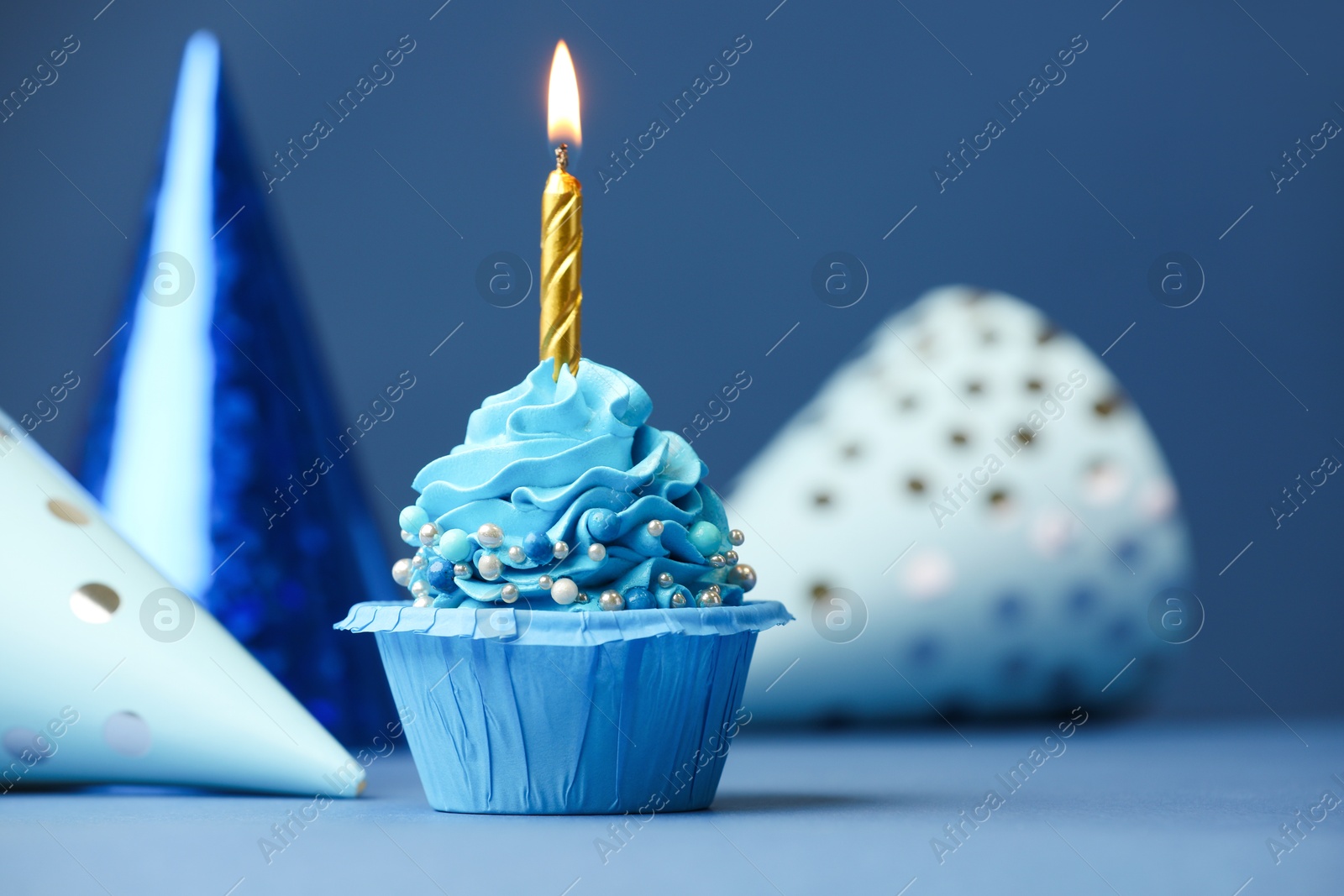 Photo of Birthday cupcake with burning candle and party cones on blue table