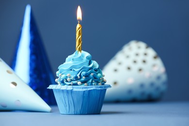 Photo of Birthday cupcake with burning candle and party cones on blue table