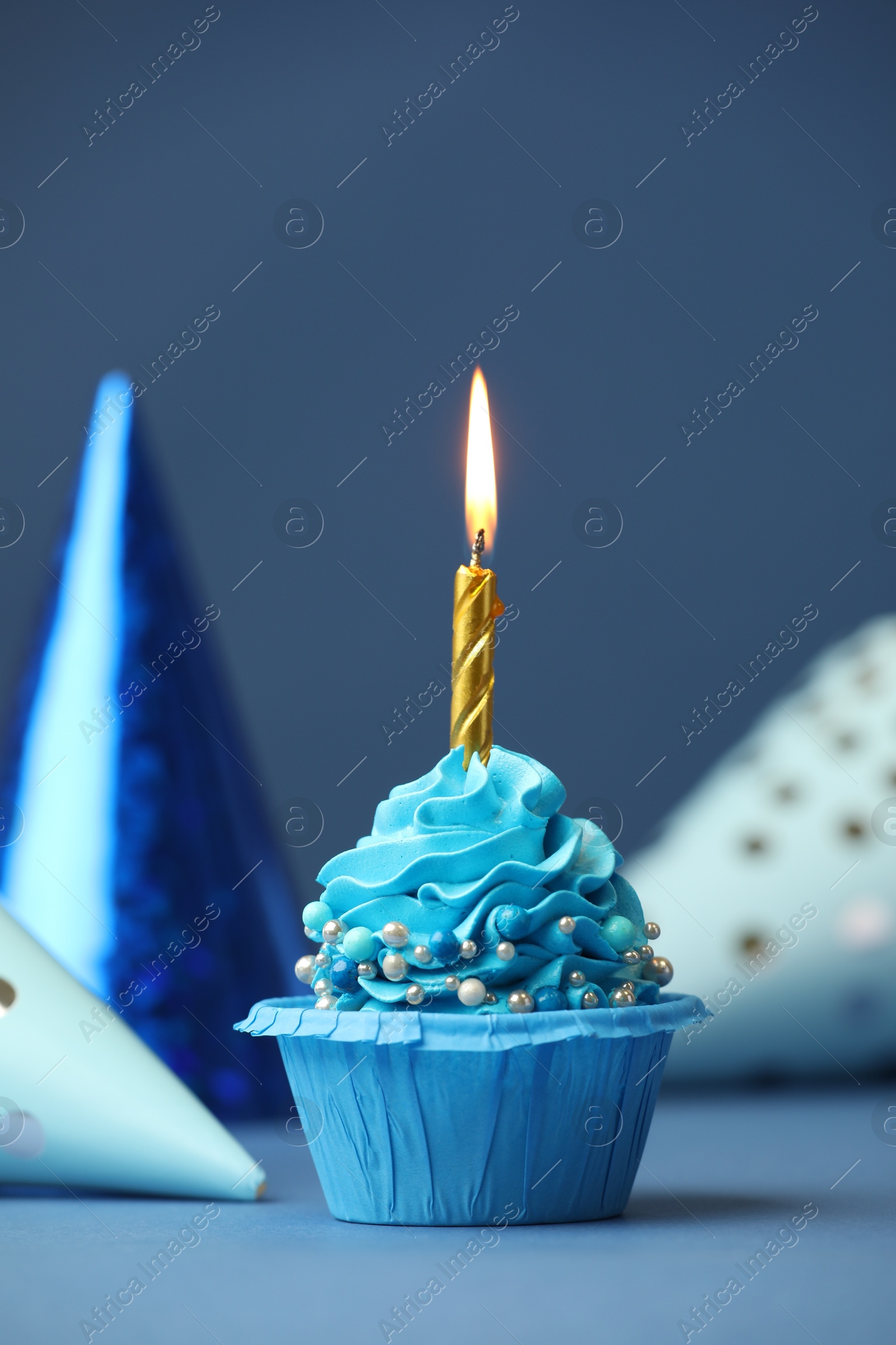 Photo of Birthday cupcake with burning candle and party cones on blue table