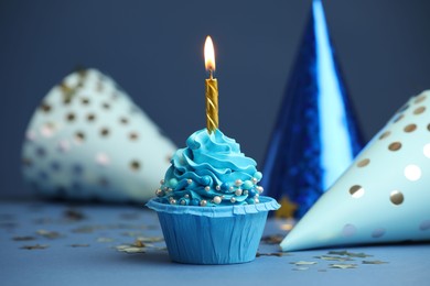 Photo of Birthday cupcake with burning candle and party cones on blue table