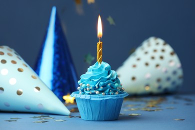 Photo of Birthday cupcake with burning candle and party cones on blue table