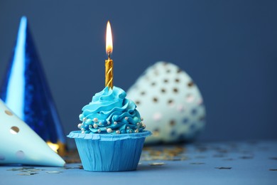 Photo of Birthday cupcake with burning candle and party cones on blue table