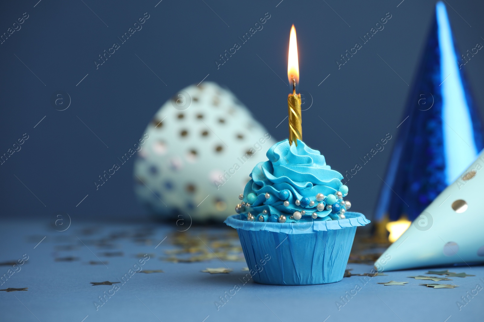 Photo of Birthday cupcake with burning candle and party cones on blue table