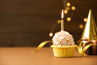 Photo of Birthday cupcake with burning candle on brown table against blurred lights. Space for text