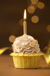 Photo of Birthday cupcake with burning candle on brown table against blurred lights