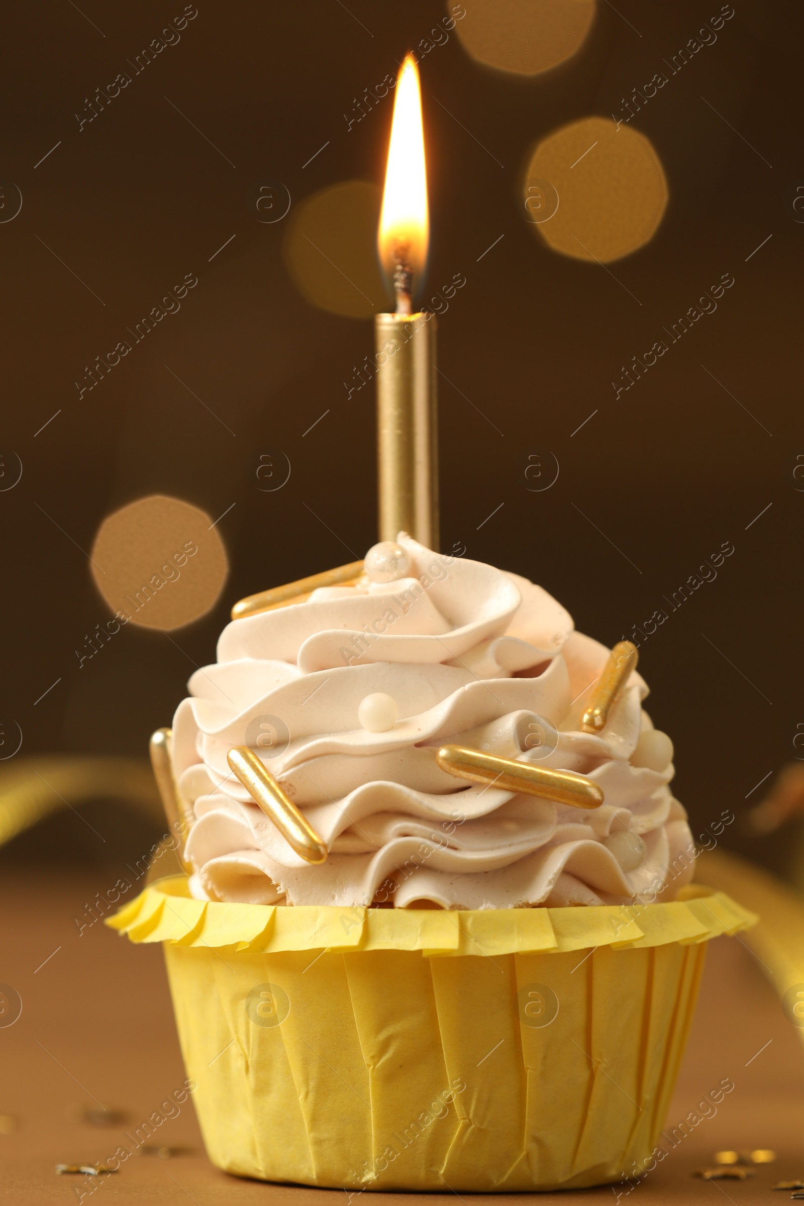 Photo of Birthday cupcake with burning candle on brown table against blurred lights