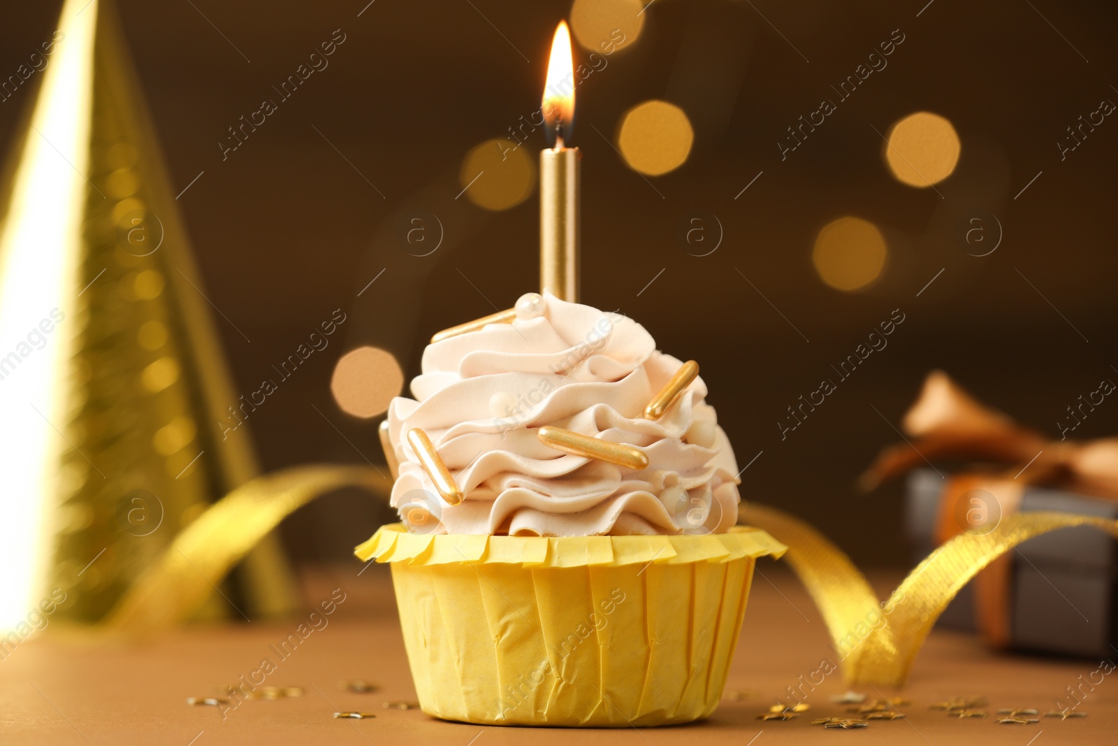 Photo of Birthday cupcake with burning candle on brown table against blurred lights