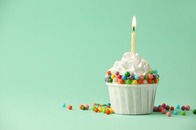 Photo of Birthday cupcake with burning candle on turquoise background. Space for text