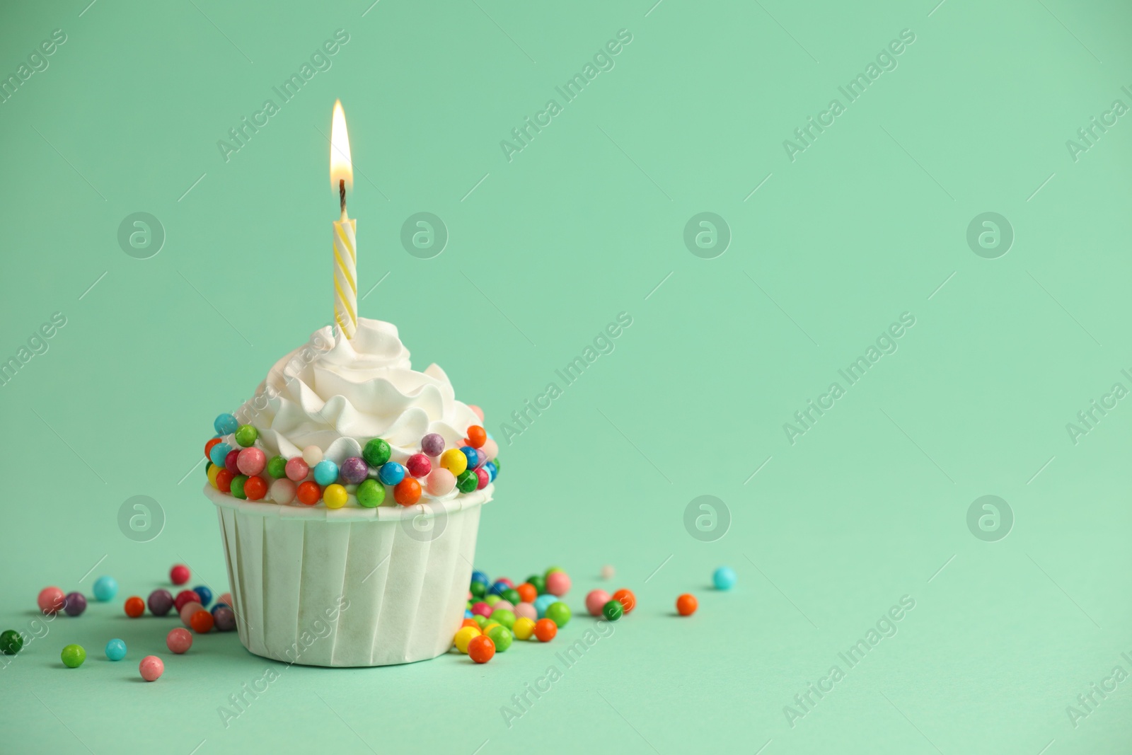 Photo of Birthday cupcake with burning candle on turquoise background. Space for text