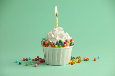 Photo of Birthday cupcake with burning candle on turquoise background