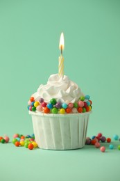 Photo of Birthday cupcake with burning candle on turquoise background