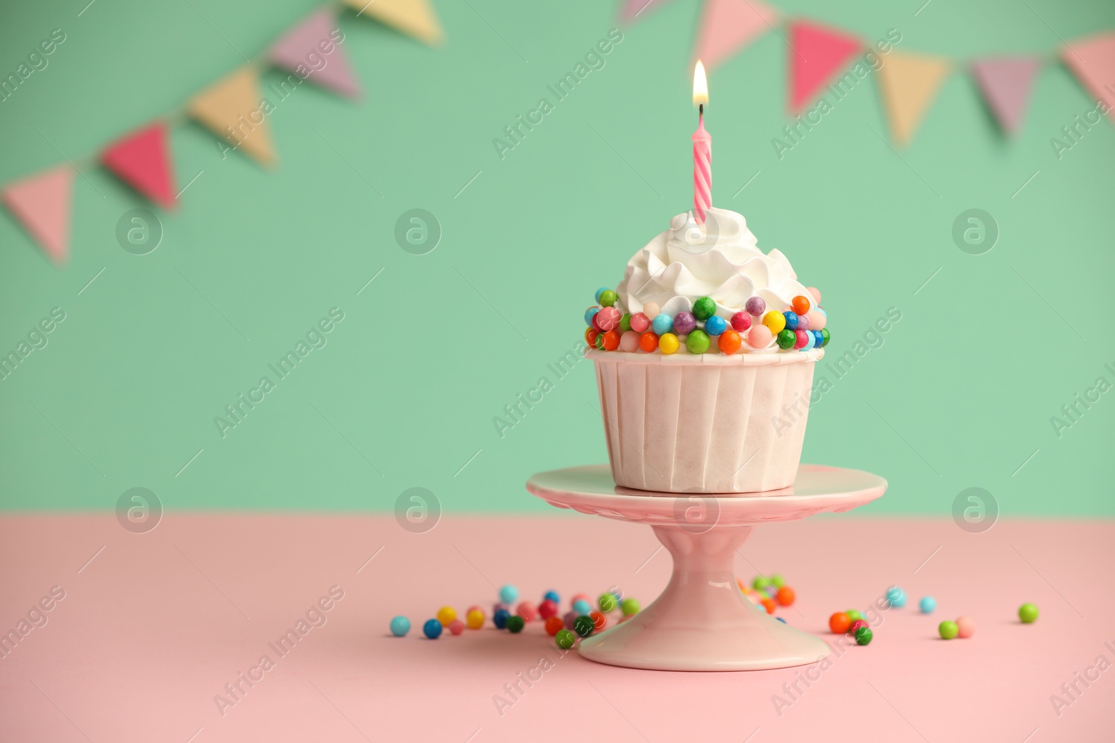 Photo of Birthday cupcake with burning candle on pink table. Space for text