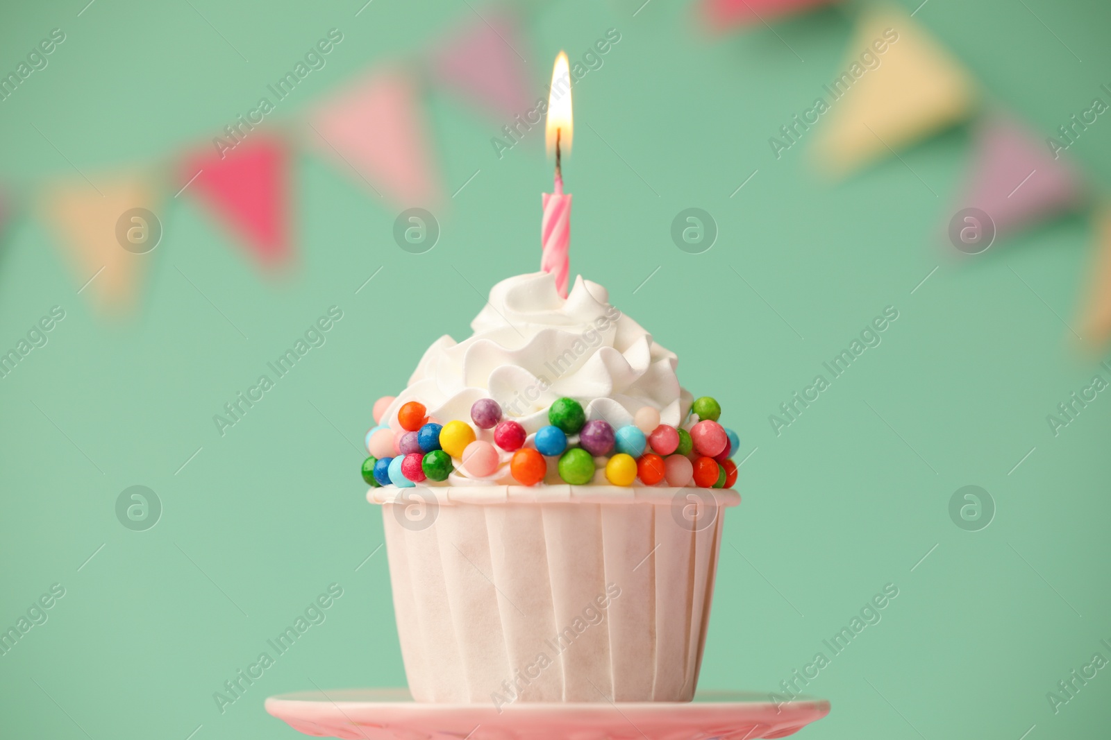 Photo of Birthday cupcake with burning candle on cake stand against turquoise background