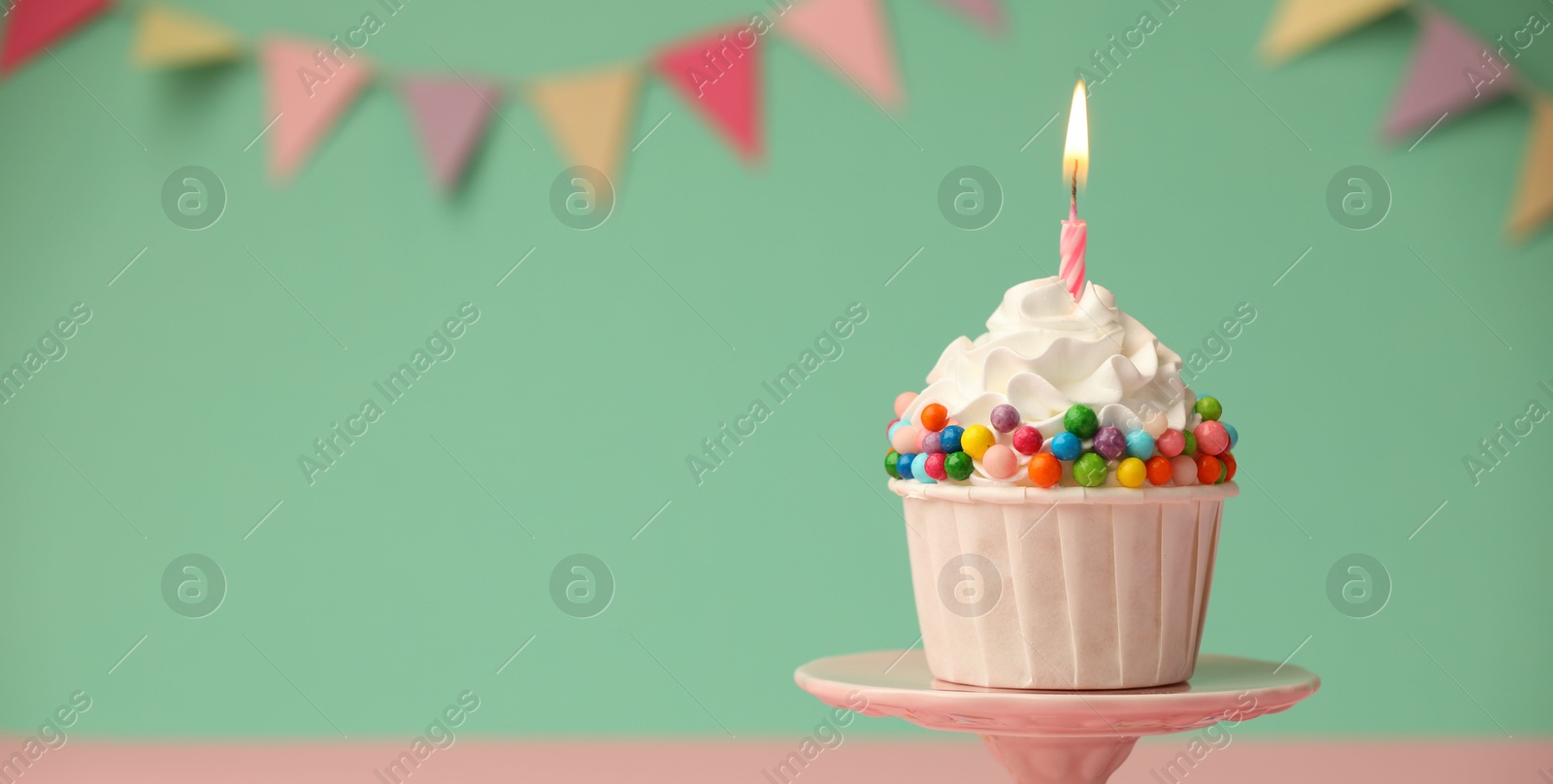 Photo of Birthday cupcake with burning candle on cake stand against turquoise background. Space for text