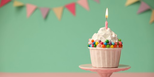 Photo of Birthday cupcake with burning candle on cake stand against turquoise background. Space for text