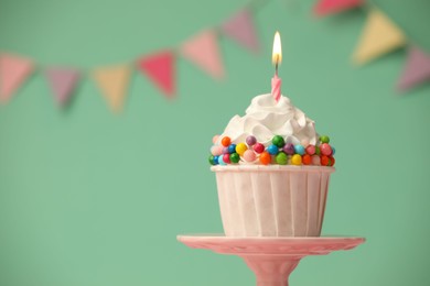 Photo of Birthday cupcake with burning candle on cake stand against turquoise background. Space for text