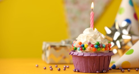 Photo of Birthday cupcake with burning candle and party cone on yellow table. Space for text