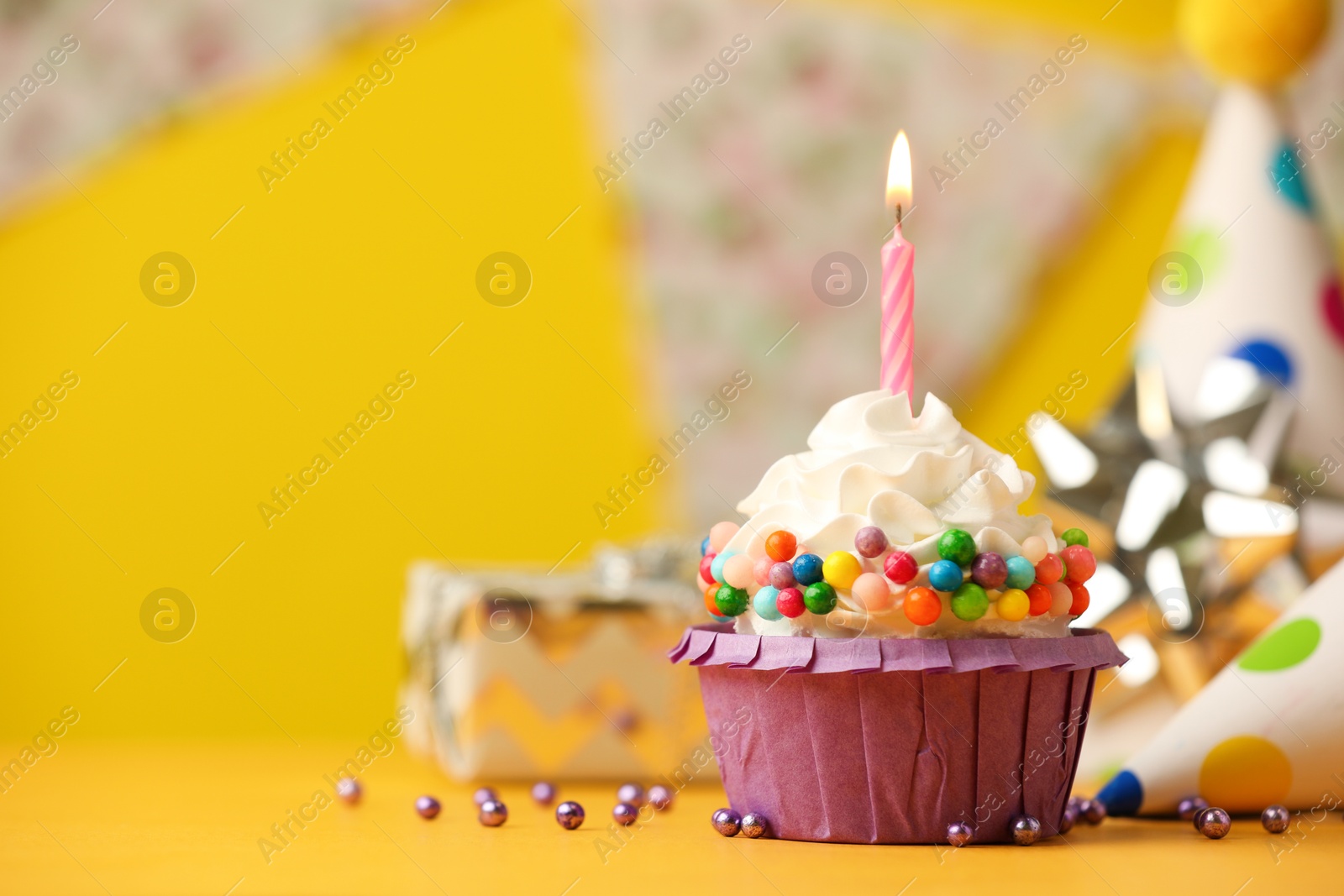 Photo of Birthday cupcake with burning candle on yellow table. Space for text