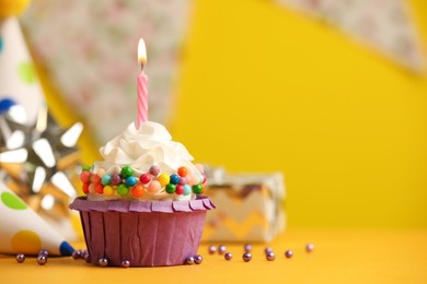 Photo of Birthday cupcake with burning candle on yellow table. Space for text