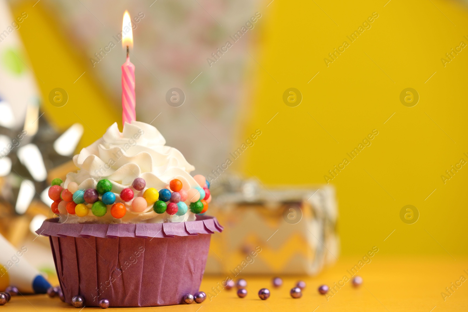 Photo of Birthday cupcake with burning candle on yellow table. Space for text