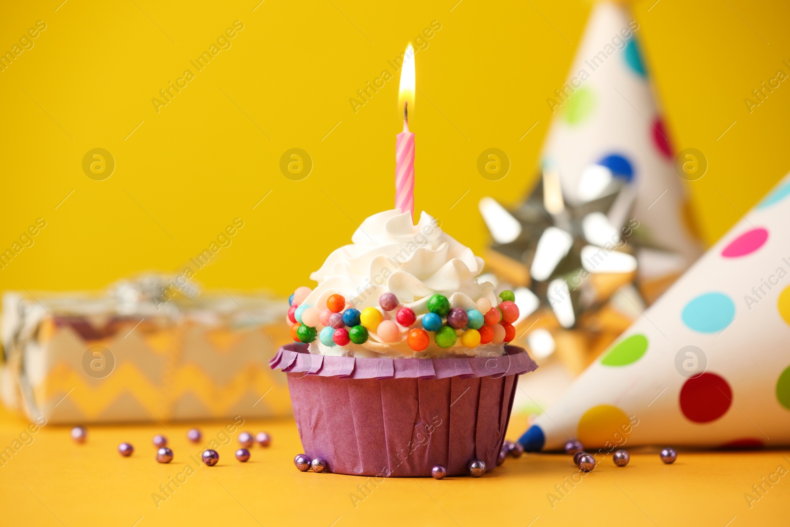 Photo of Birthday cupcake with burning candle and party cone on yellow table