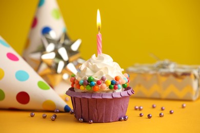 Photo of Birthday cupcake with burning candle and party cone on yellow table