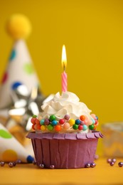 Photo of Birthday cupcake with burning candle on yellow table