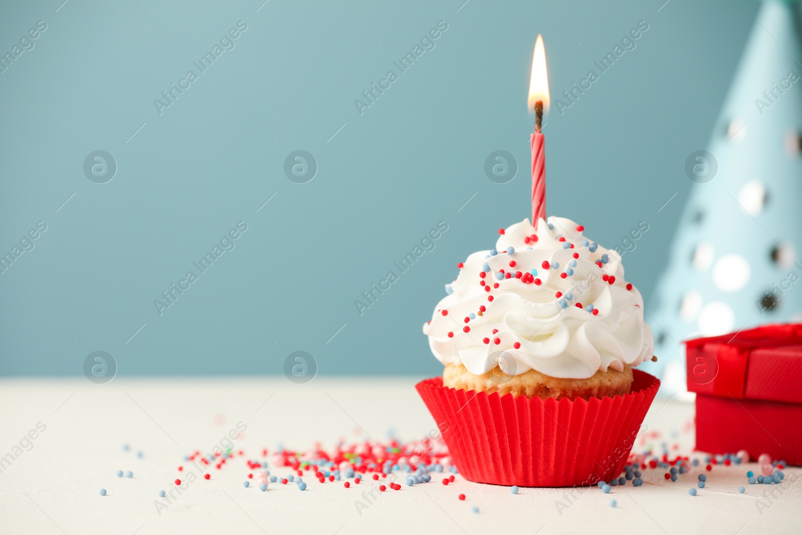 Photo of Birthday cupcake with burning candle, gift and party cone on white table. Space for text