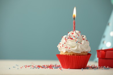 Photo of Birthday cupcake with burning candle, gift and party cone on white table. Space for text