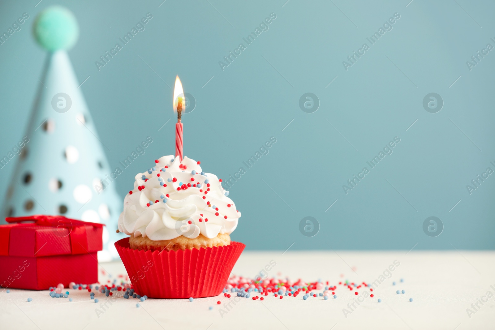 Photo of Birthday cupcake with burning candle, gift and party cone on white table. Space for text