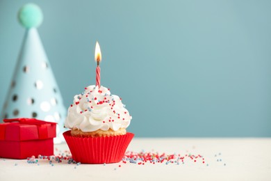 Photo of Birthday cupcake with burning candle, gift and party cone on white table. Space for text