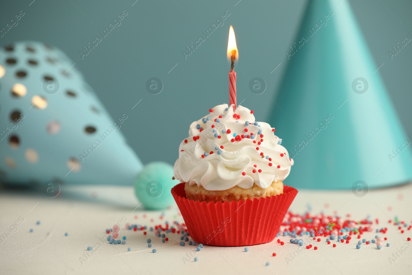 Photo of Birthday cupcake with burning candle and party cones on white table