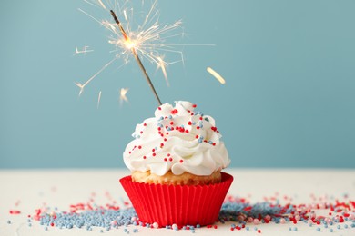 Photo of Birthday cupcake with burning sparkler on white table