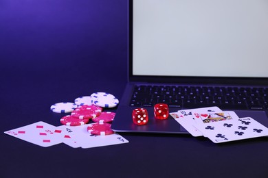 Photo of Online poker. Playing cards, chips, dice and laptop on dark table, closeup