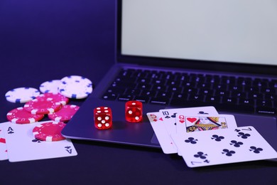 Photo of Online poker. Playing cards, chips, dice and laptop on dark table, closeup