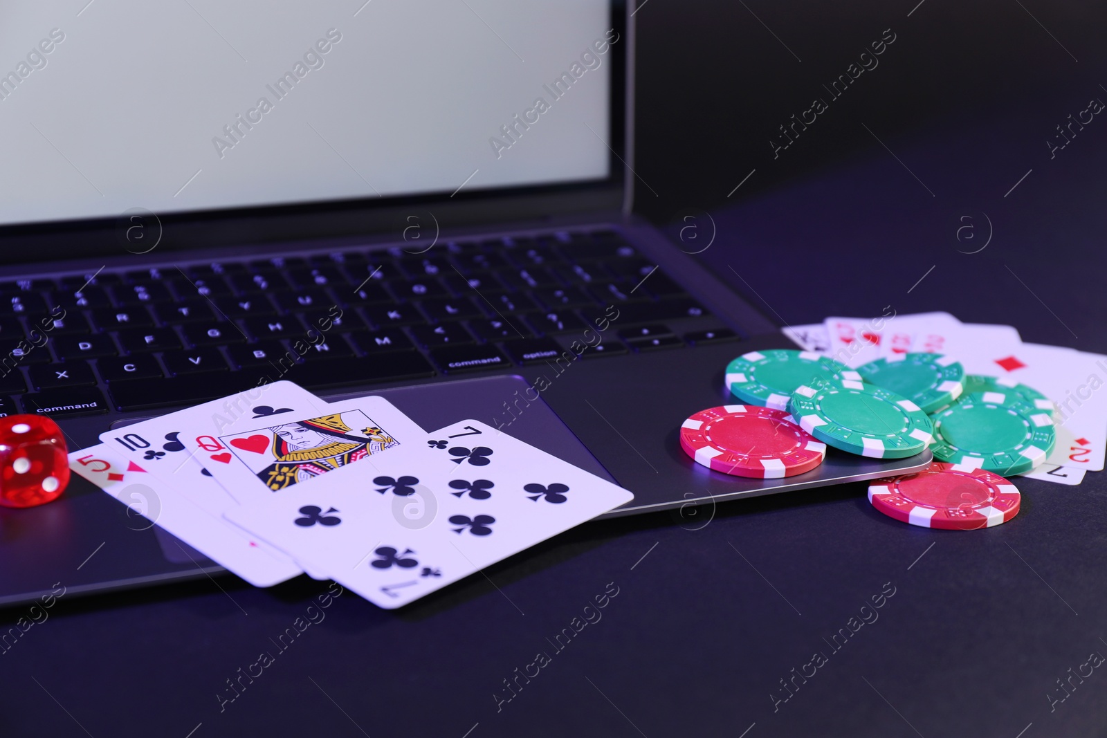 Photo of Online poker. Playing cards, chips, dice and laptop on dark table, closeup