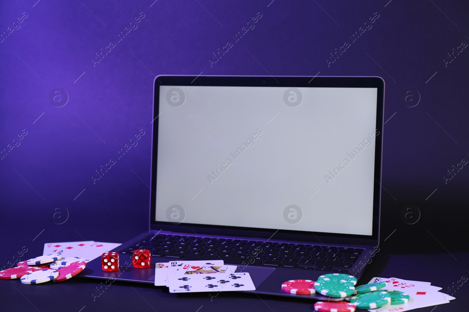 Photo of Online poker. Playing cards, chips, dice and laptop on dark table