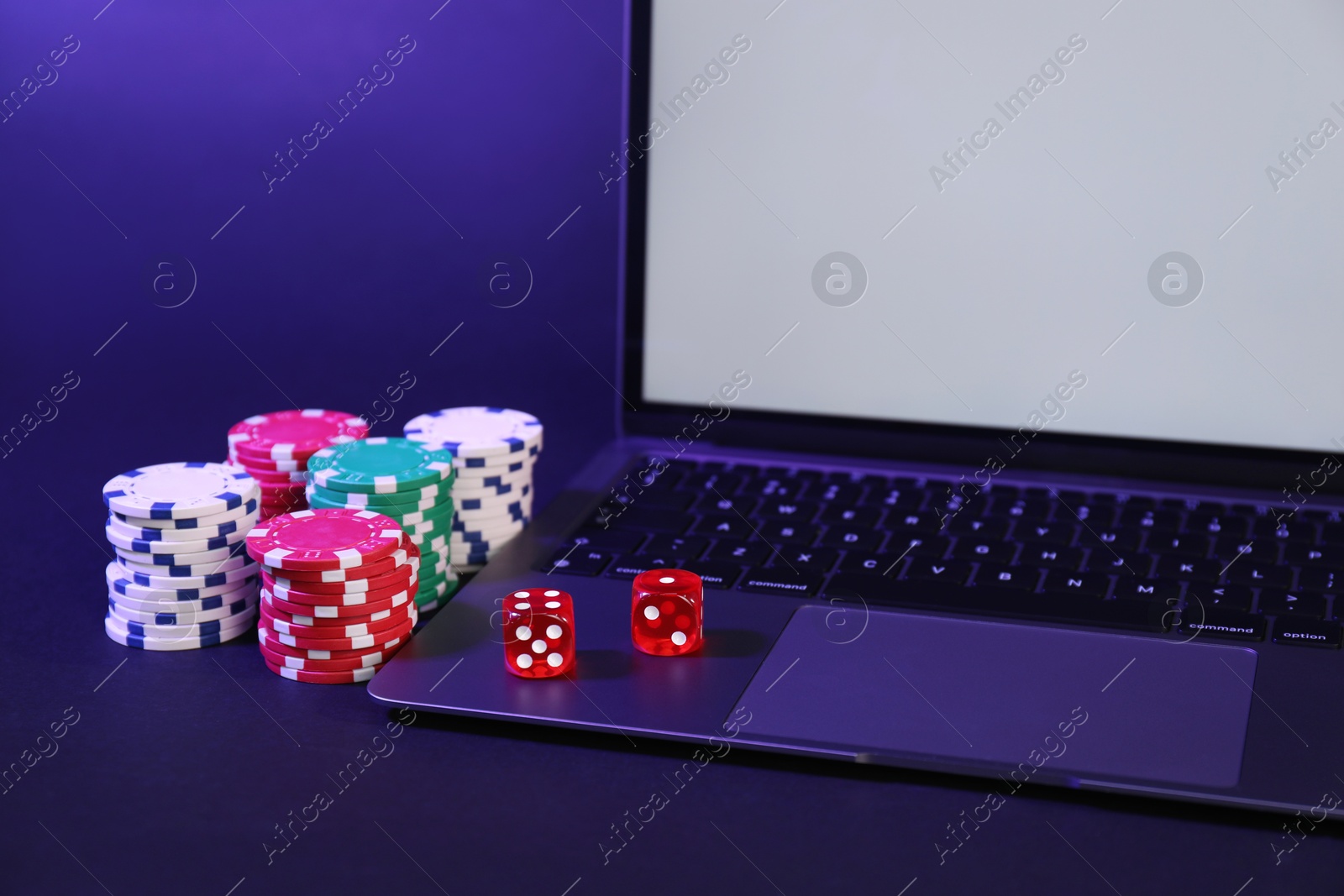 Photo of Online poker. Chips, dice and laptop on dark table