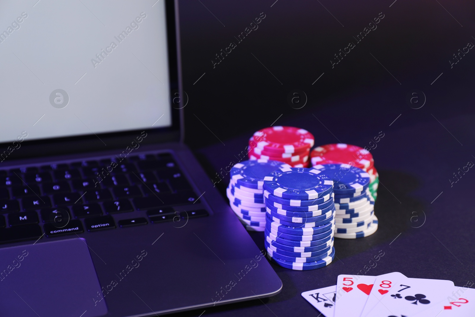 Photo of Online poker. Playing cards, chips and laptop on dark table, closeup