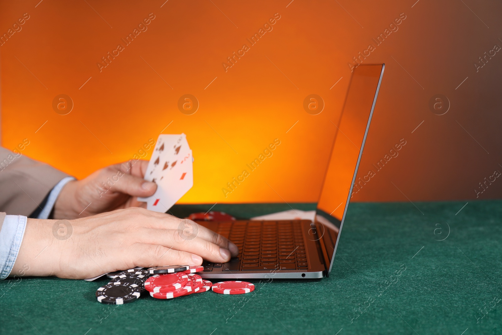 Photo of Online poker. Man holding playing cards and using laptop at green table, closeup