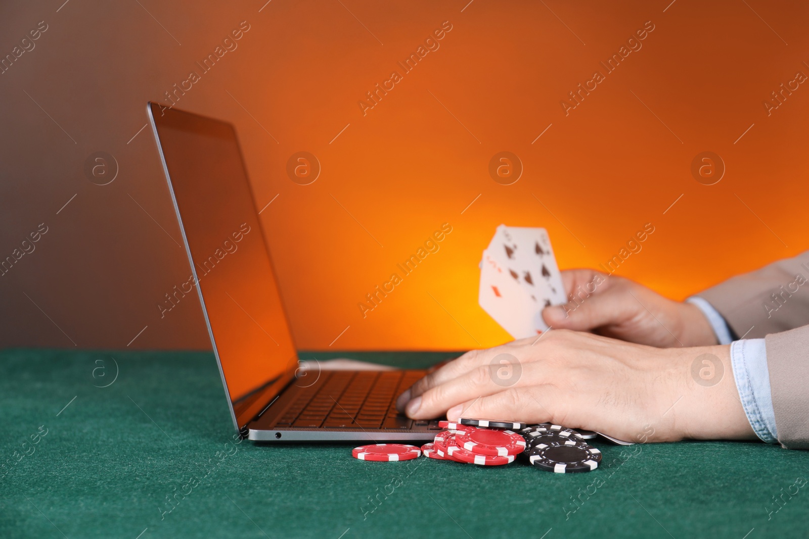 Photo of Online poker. Man holding playing cards and using laptop at green table, closeup