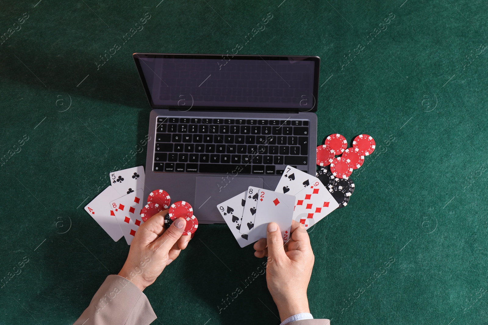 Photo of Online poker. Man holding playing cards and chips at green table with laptop, top view