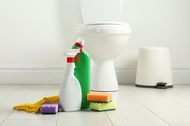 Photo of Toilet cleaners, sponges and gloves on floor in bathroom