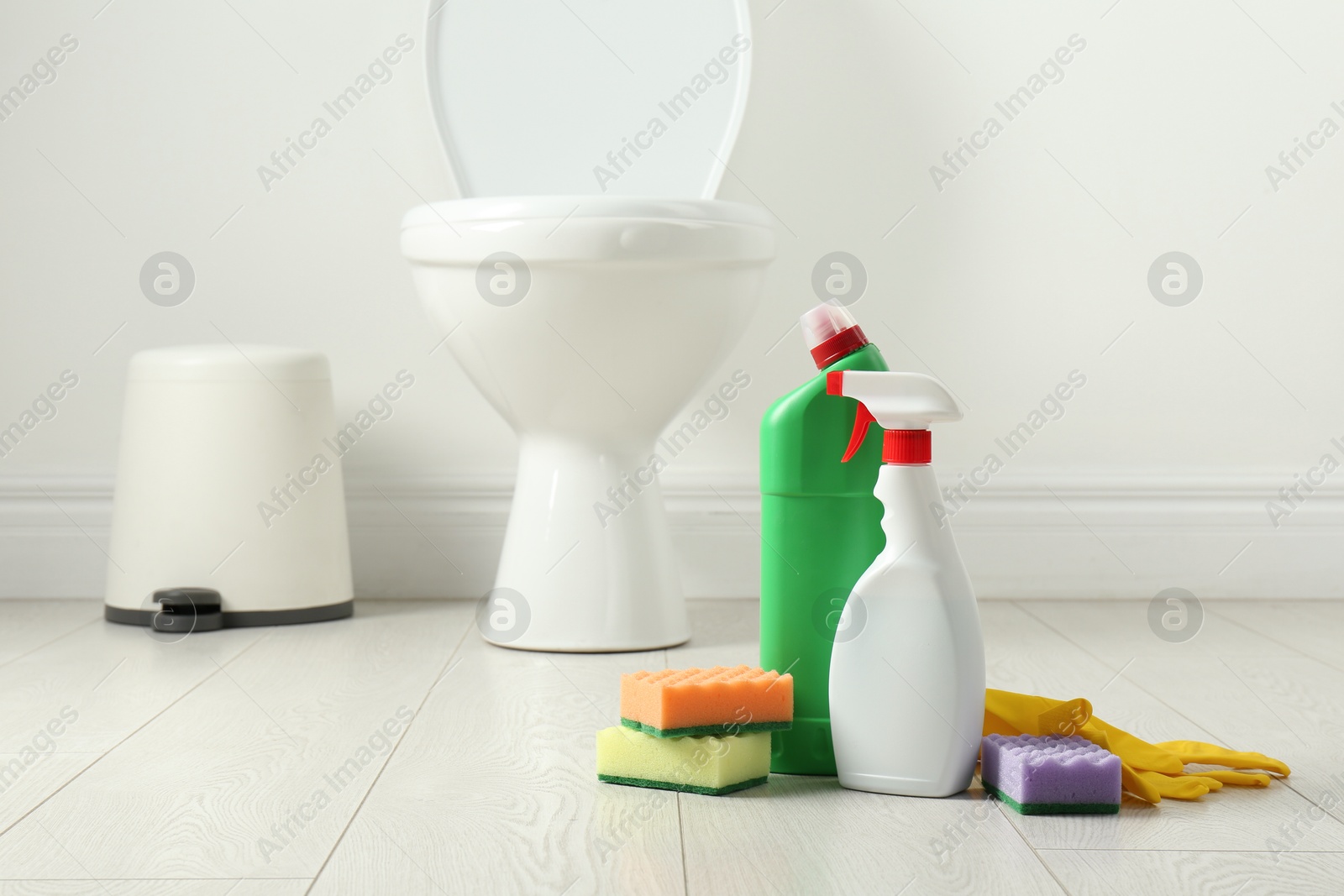 Photo of Toilet cleaners, sponges and gloves on floor in bathroom