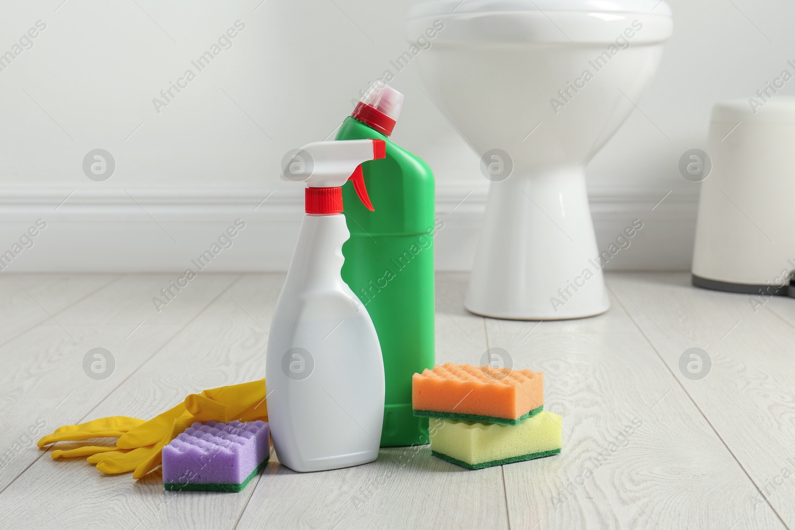 Photo of Toilet cleaners, sponges and gloves on floor in bathroom