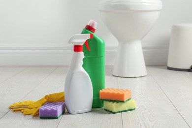 Photo of Toilet cleaners, sponges and gloves on floor in bathroom