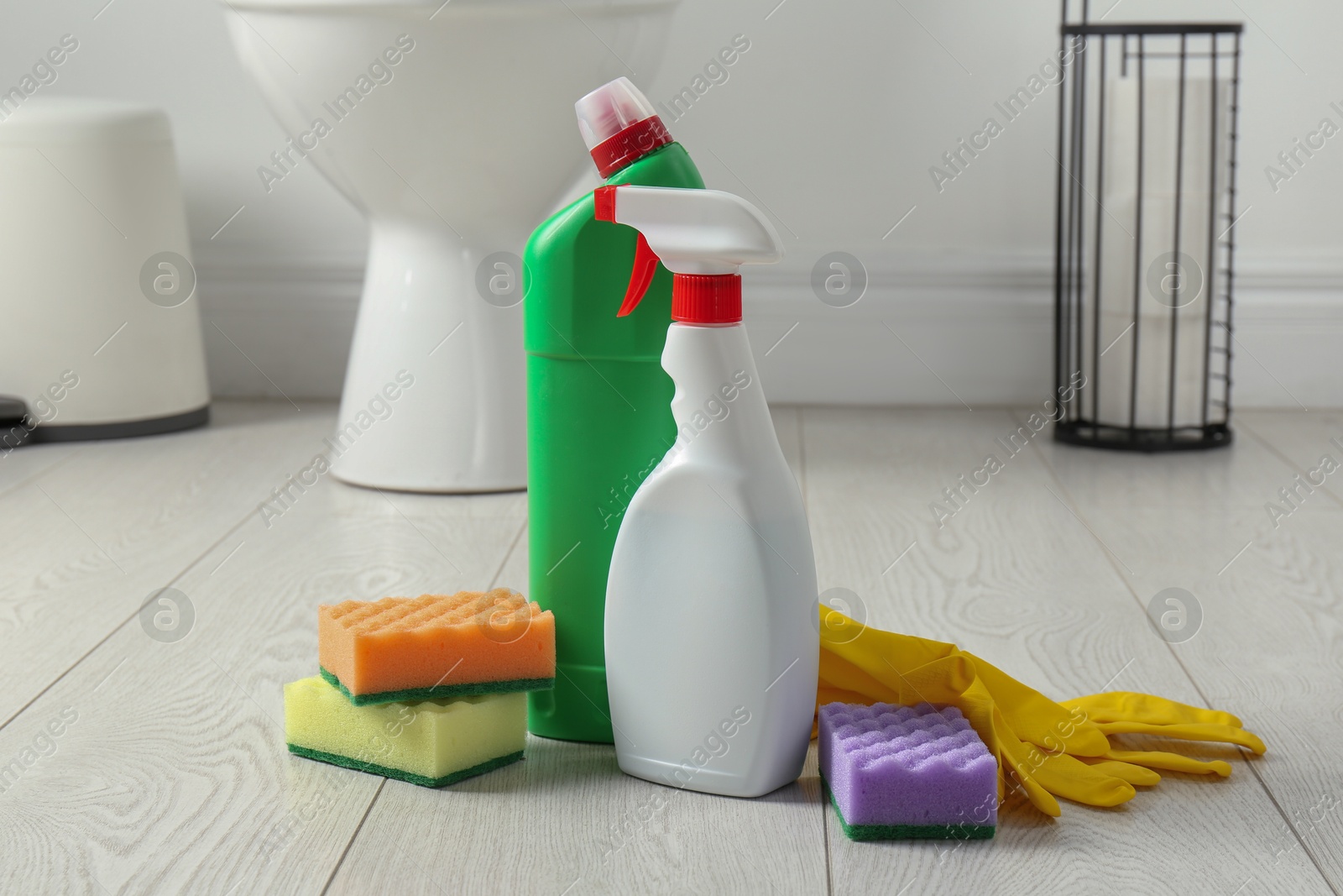 Photo of Toilet cleaners, sponges and gloves on floor in bathroom