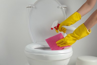 Photo of Woman with spray and rag cleaning toilet seat in bathroom, closeup